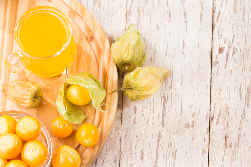 Goldenberries and a pitcher of goldenberry juice on a wooden board during the day.